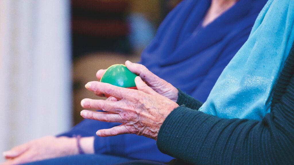 Manos de un paciente realizando ejercicios de fisioterapia post-ictus con una pelota para mejorar fuerza y coordinación.